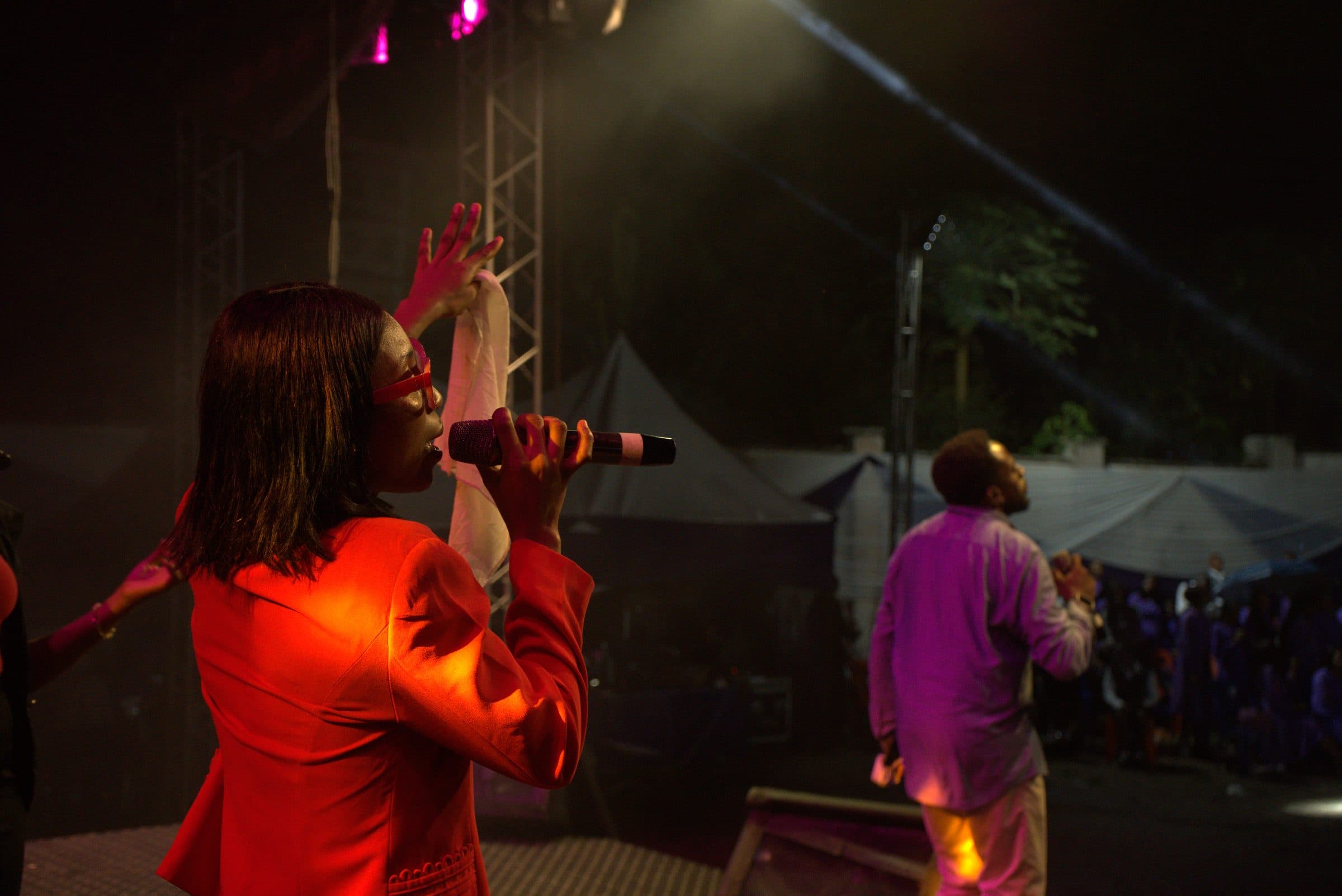 A vocalist singing under red stage light, hand raised.